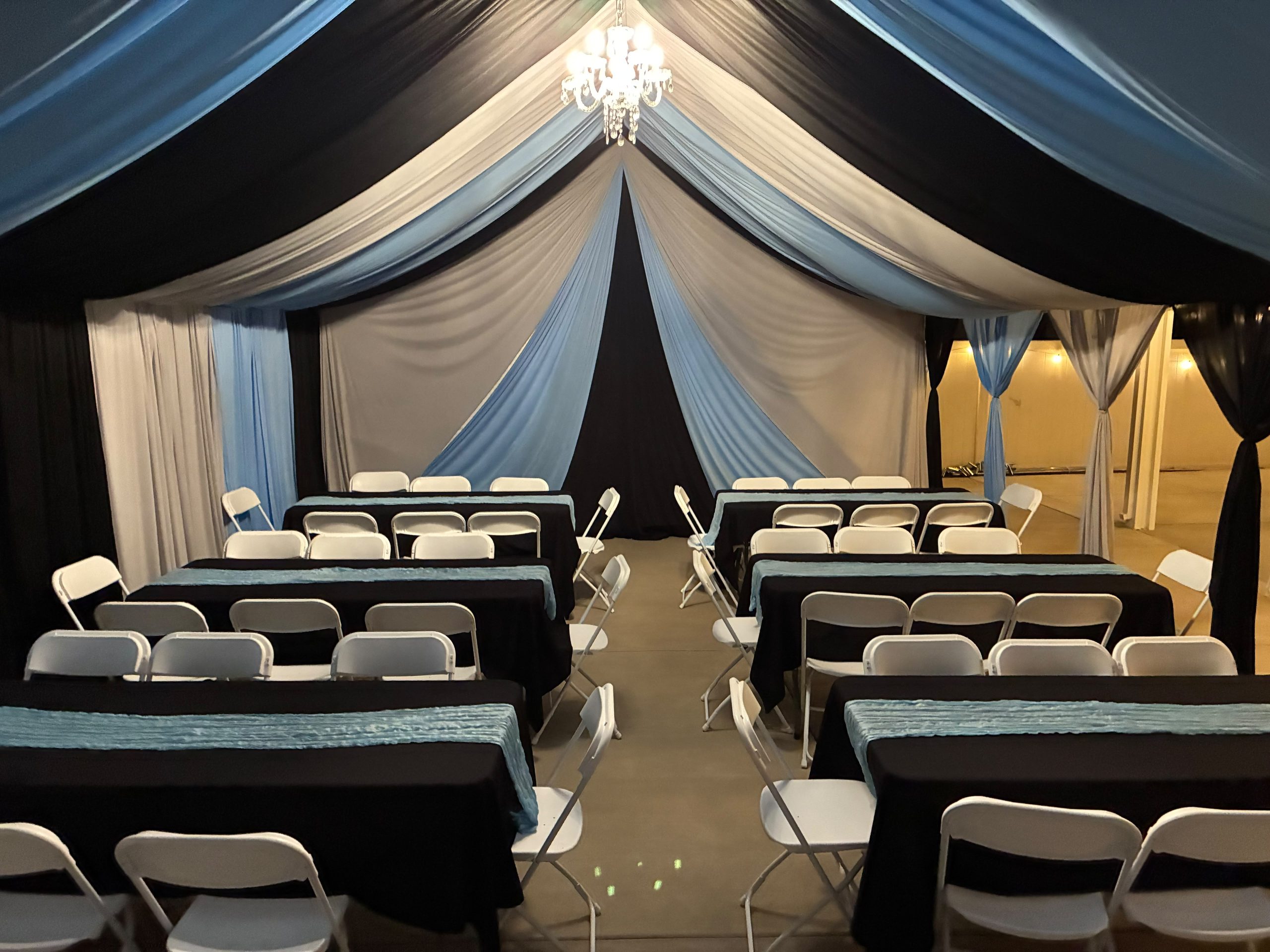 Real Loren's Party Rentals Black, white and blue draped tent with chandelier. Style inspiration, not a size-specific product photograph.