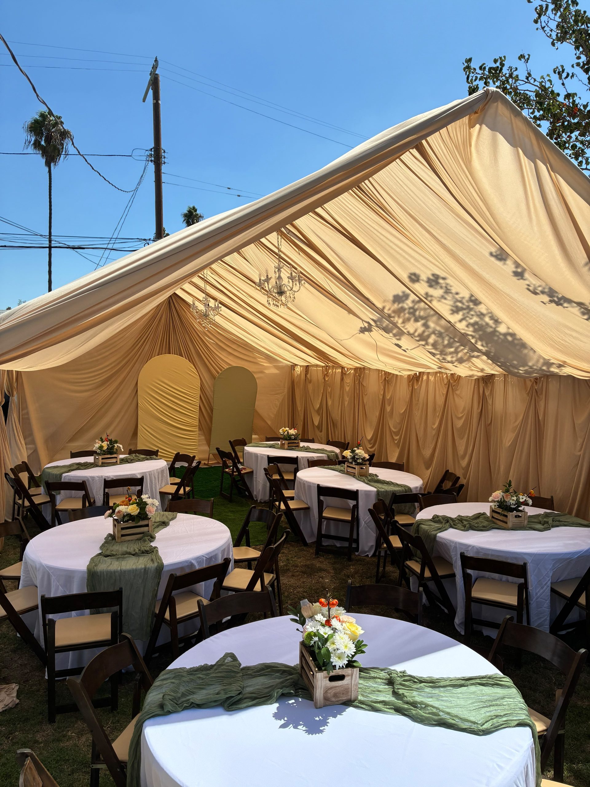 Champagne and ivory draped event tent with round banquet tables, chairs and flower arrangements by Loren's Party Rentals